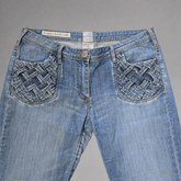Blue jeans with woven patterns on the back pockets against a gray background